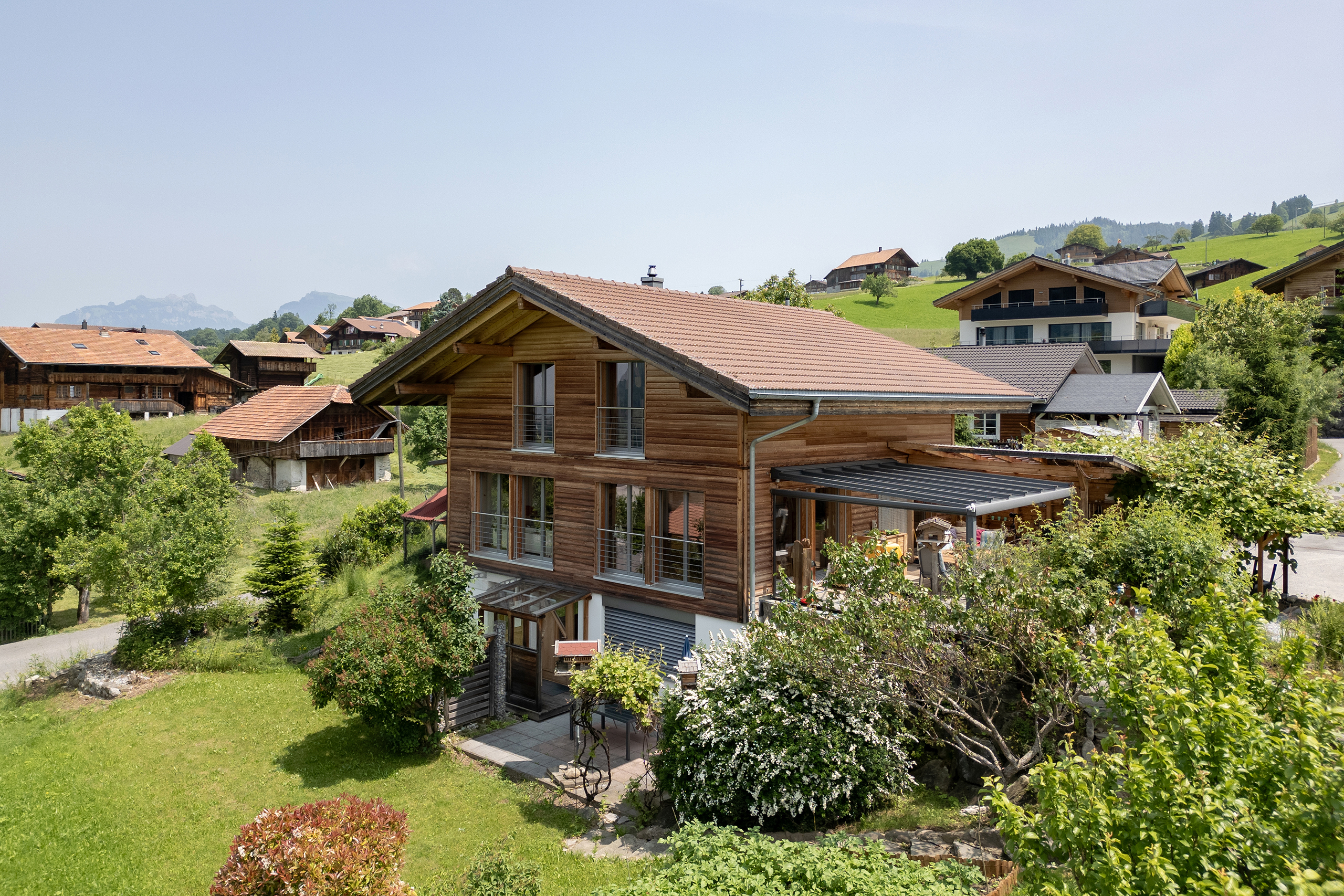 Blick aus südwest auf das freistehende Holzchalet in Reichenbach im Kandertal. Überdachte Terrasse und Nebengebäude seitlich des Haupthauses.