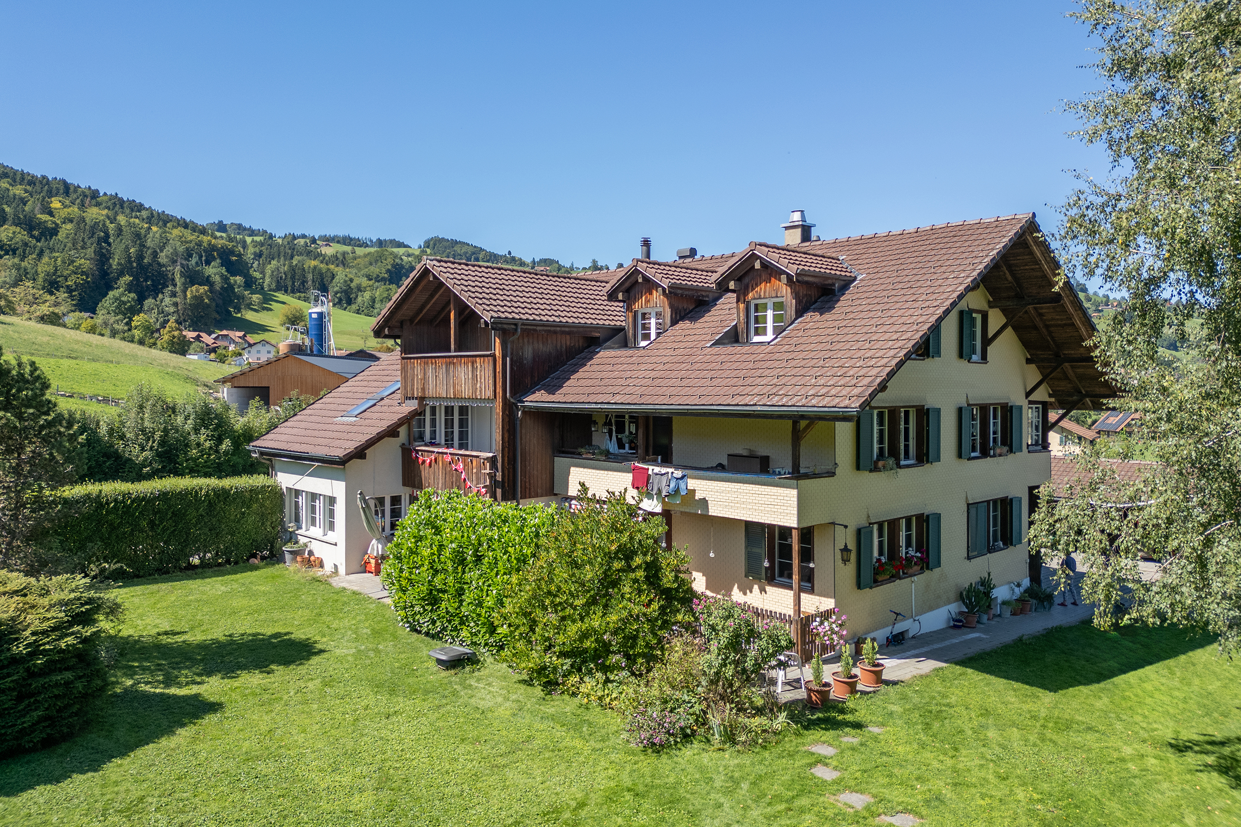 Blick auf ein Mehrfamilienhaus mit grossem Umschwung und fünf Wohnungen. Im Hintergrund steht das Gantrischgebirge.
