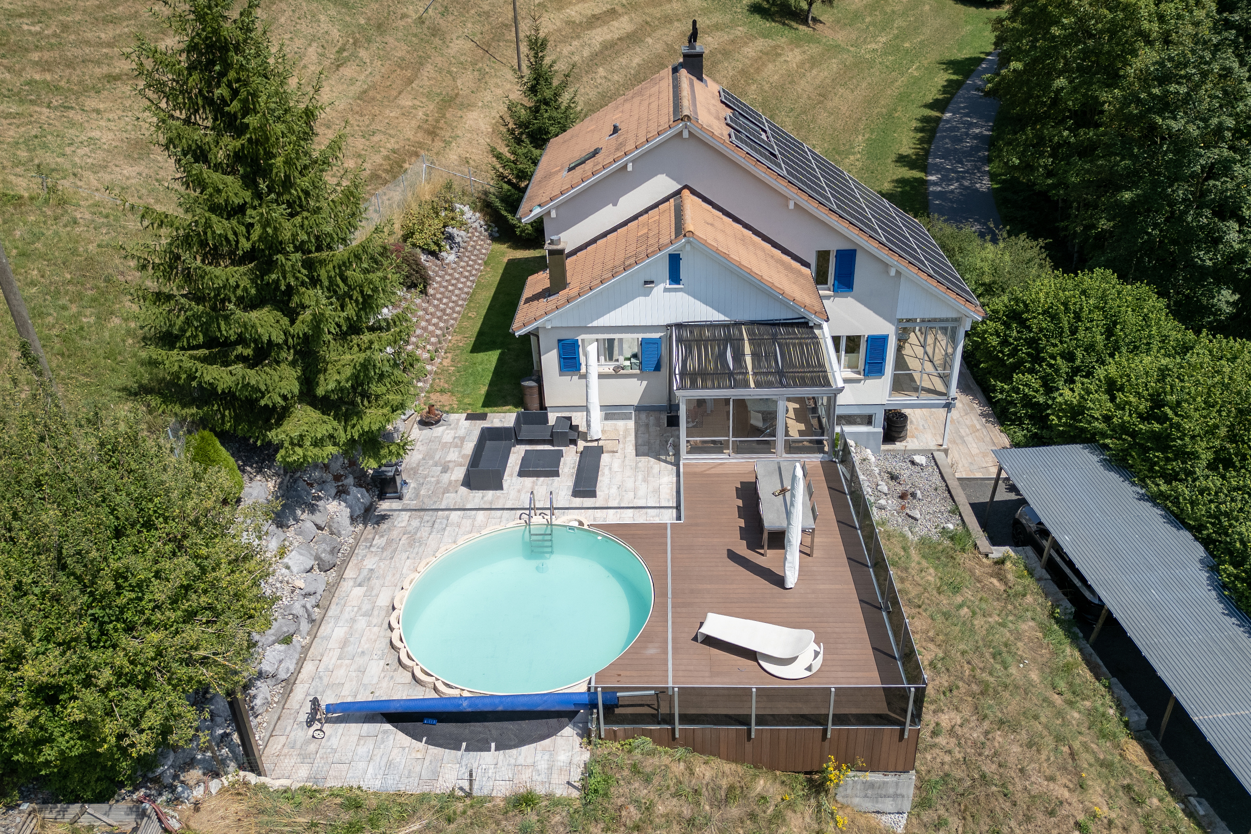Drohnenfoto eines Hauses in Guggisberg mit Sicht von Westen her auf die Terrasse mit Pool, Lounge und Gartensitzplatz.