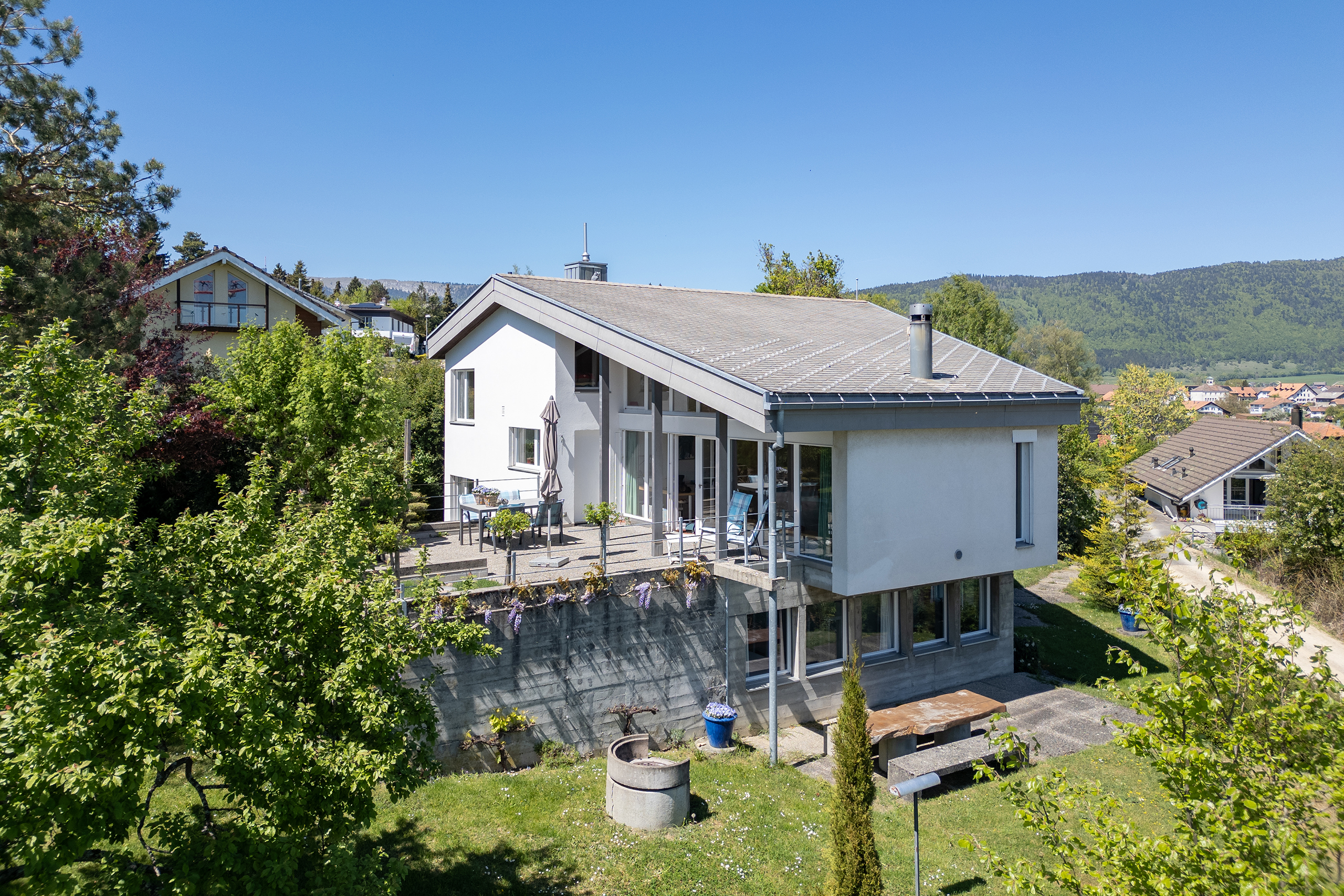 Hoch über dem Bielersee, in der Gemeinde Prêles, steht in einem Parkähnlichen Garten, ein architektonisch auffälliges Einfamilienhaus mit Einliegerwohnung.